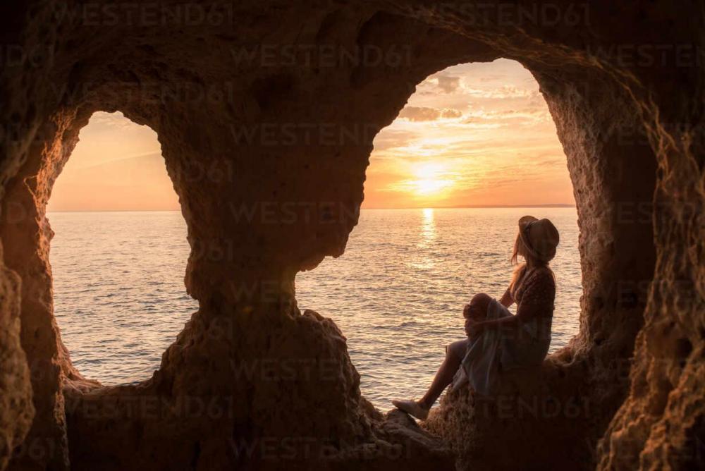 side-view-of-anonymous-female-in-hat-sitting-in-rock-looking-at-entrance-of-cave-near-sea-during-sunset-in-algar-seco-caves-in-algarve-portugal-ADSF20892.jpg