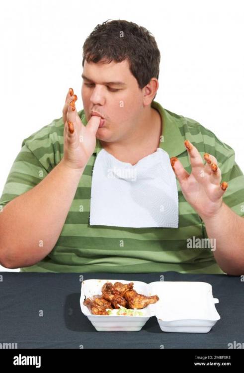 fingers-full-of-fat-an-obese-young-man-wearing-a-bib-and-siting-at-a-table-with-a-container-of-saucy-chicken-wings-and-licking-his-sauce-covered-2M8FXR3.jpg